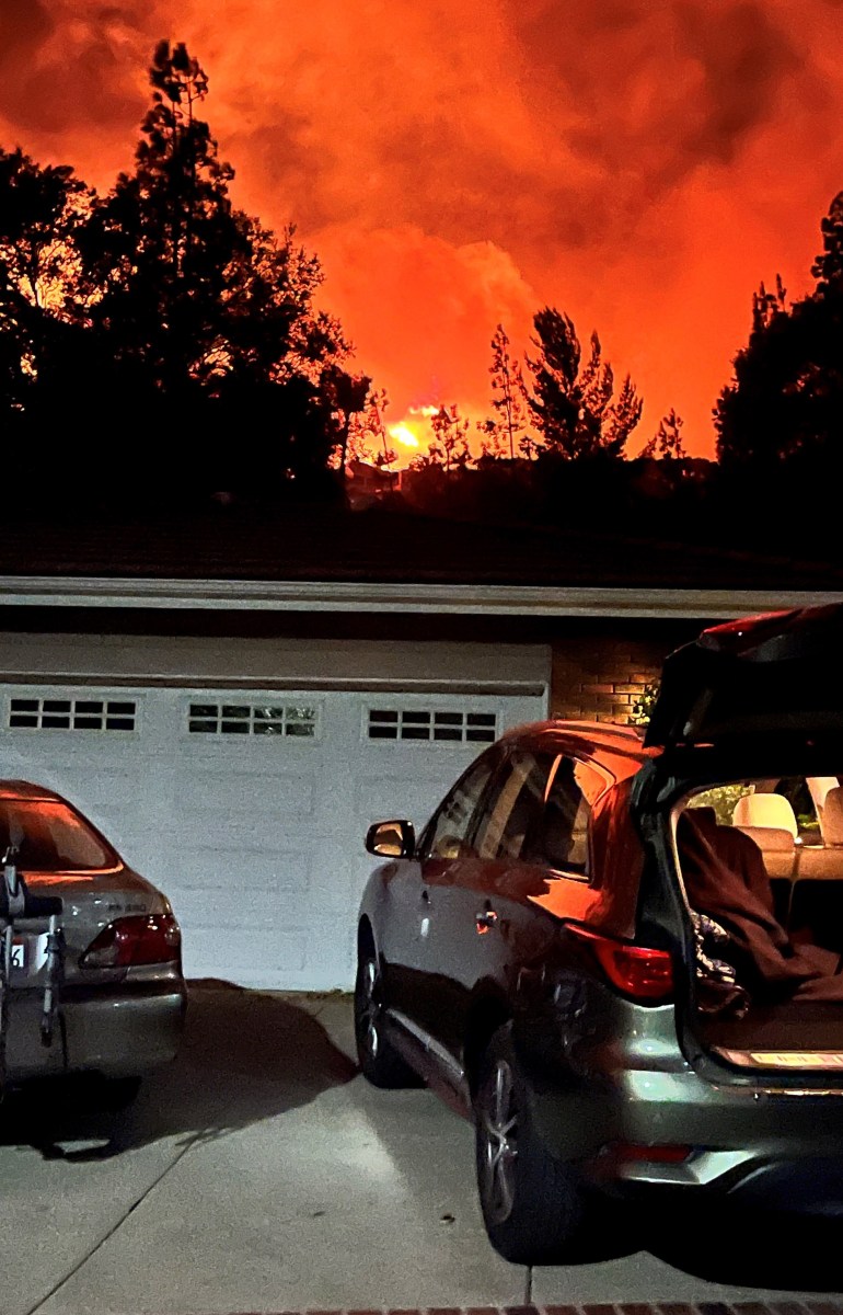 A photo showing a car in front of a home garage. The sky in the background is bright orange, set ablaze from wildfires.