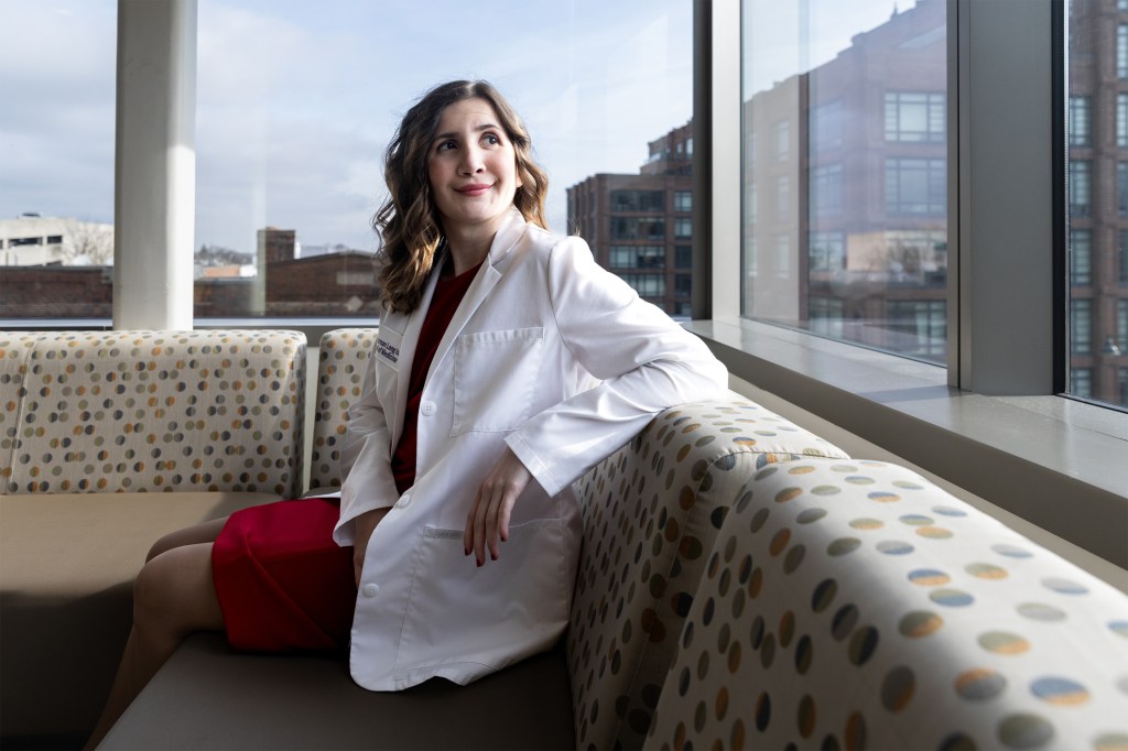 A photo of a female medical student seated by a large, windowed sitting area. She is looking over her shoulder.