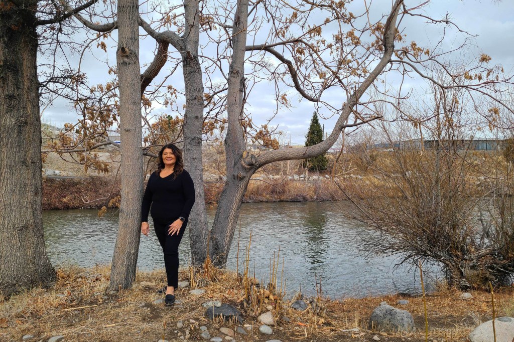 A woman stands out in a wooded area by a pond in autumn.