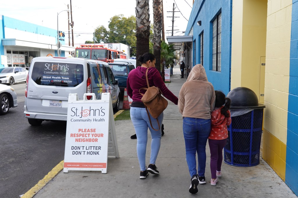 A photo of a woman walking with two kids on the sidewalk by a health clinic in California.