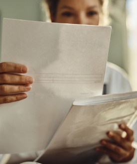 A photograph of a woman holding up a piece of paper. Her face is obstructed from view.