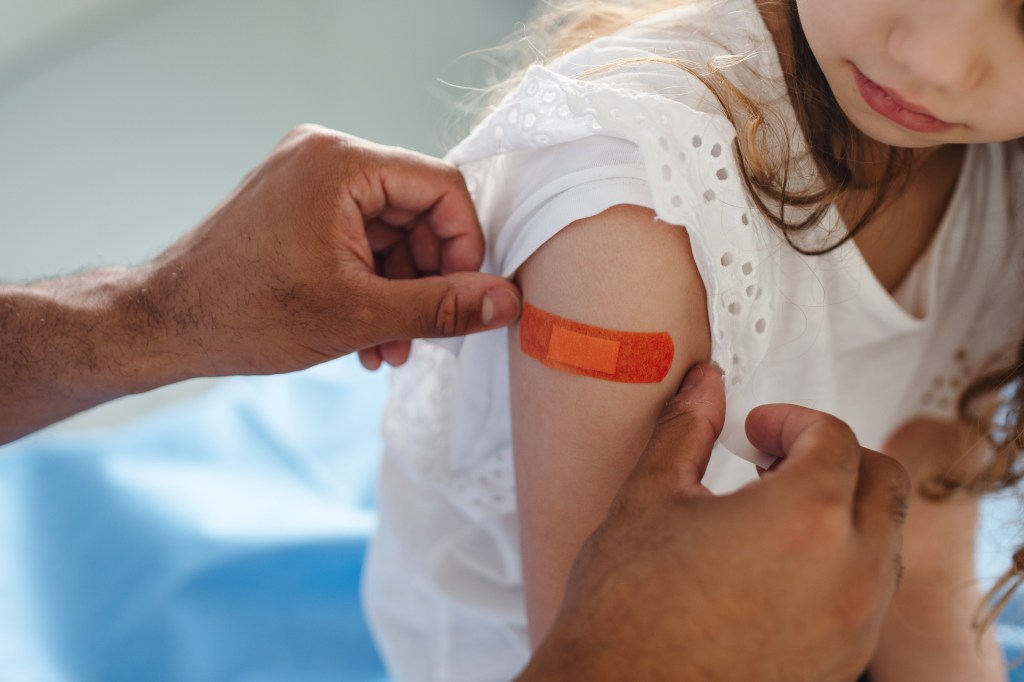 A photo of a doctor giving a little girl a bandage on her arm after getting vaccinated.