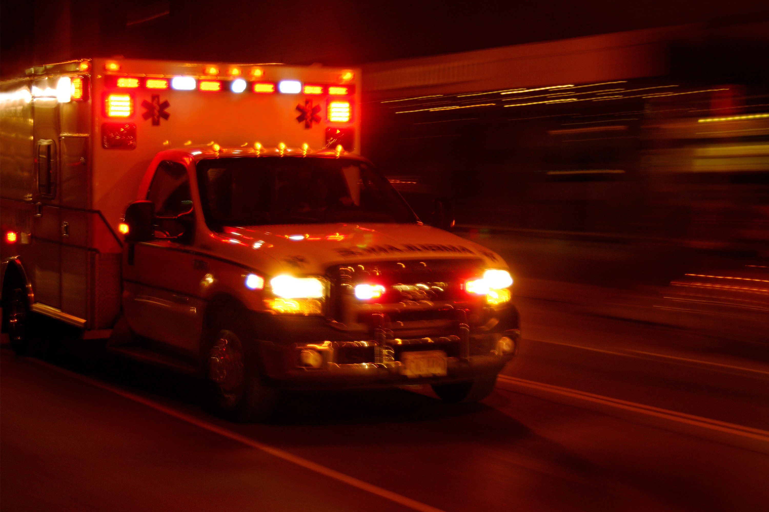 A photo of an ambulance with lights on speeding along the road at night.