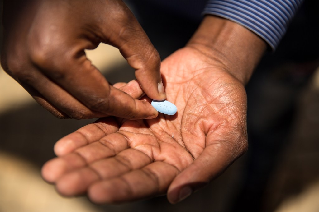 A photo of the hands of a black man holding a blue pill of PrEP medication.