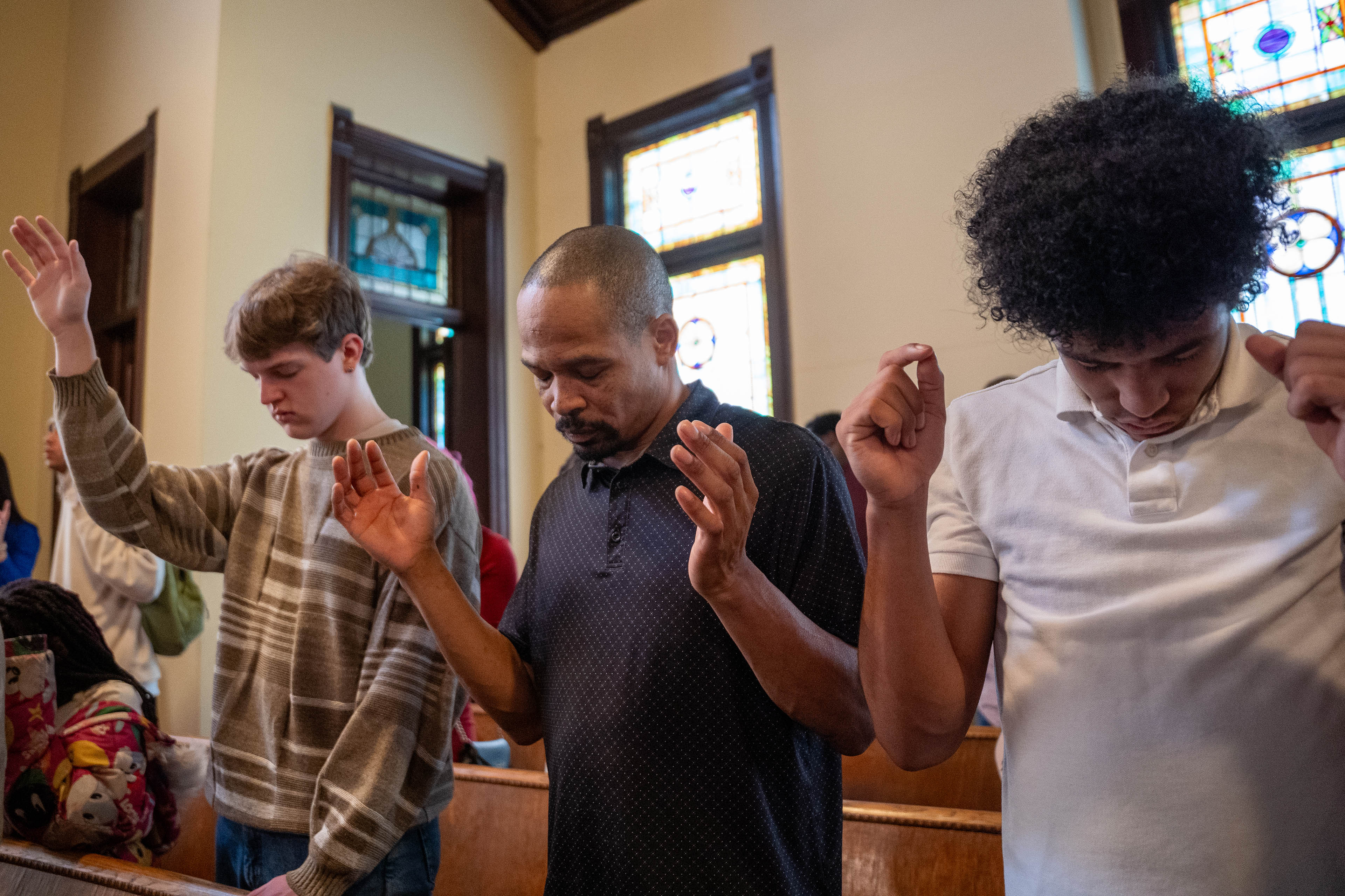 Three men stand in a pew during a church service