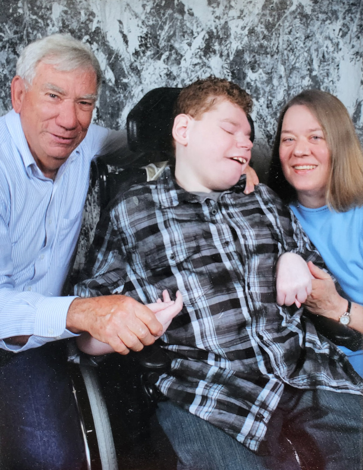 A photo of a father and mother posing for a photo with their son as a child.