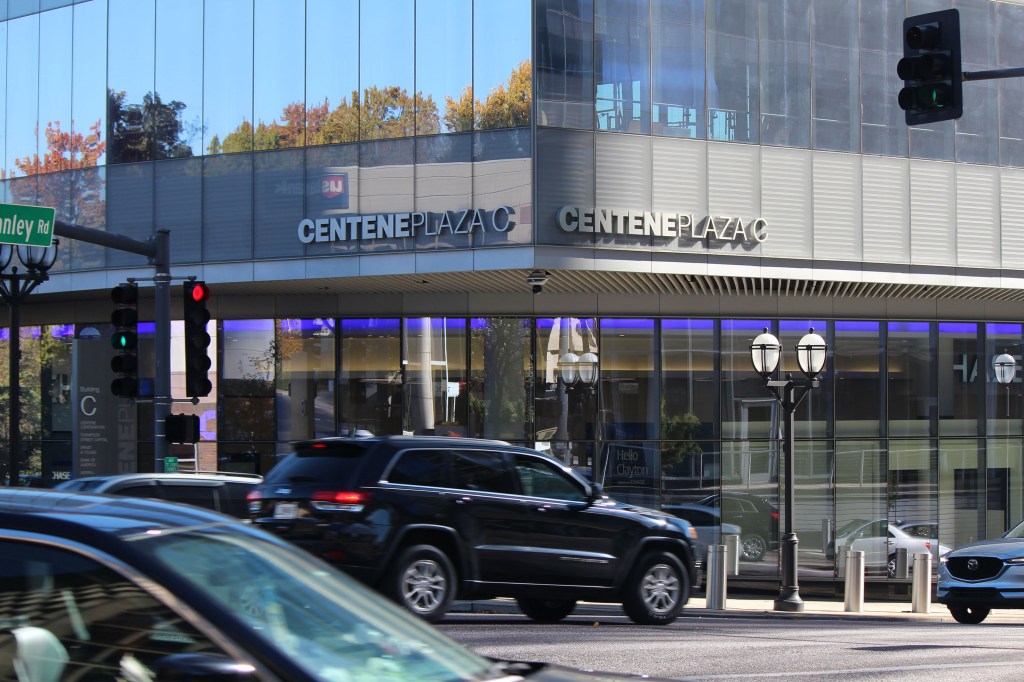 An exterior photograph of a modern office building in a metropolitan area. Cars are seen driving in front of the building labeled "Centene Plaza."