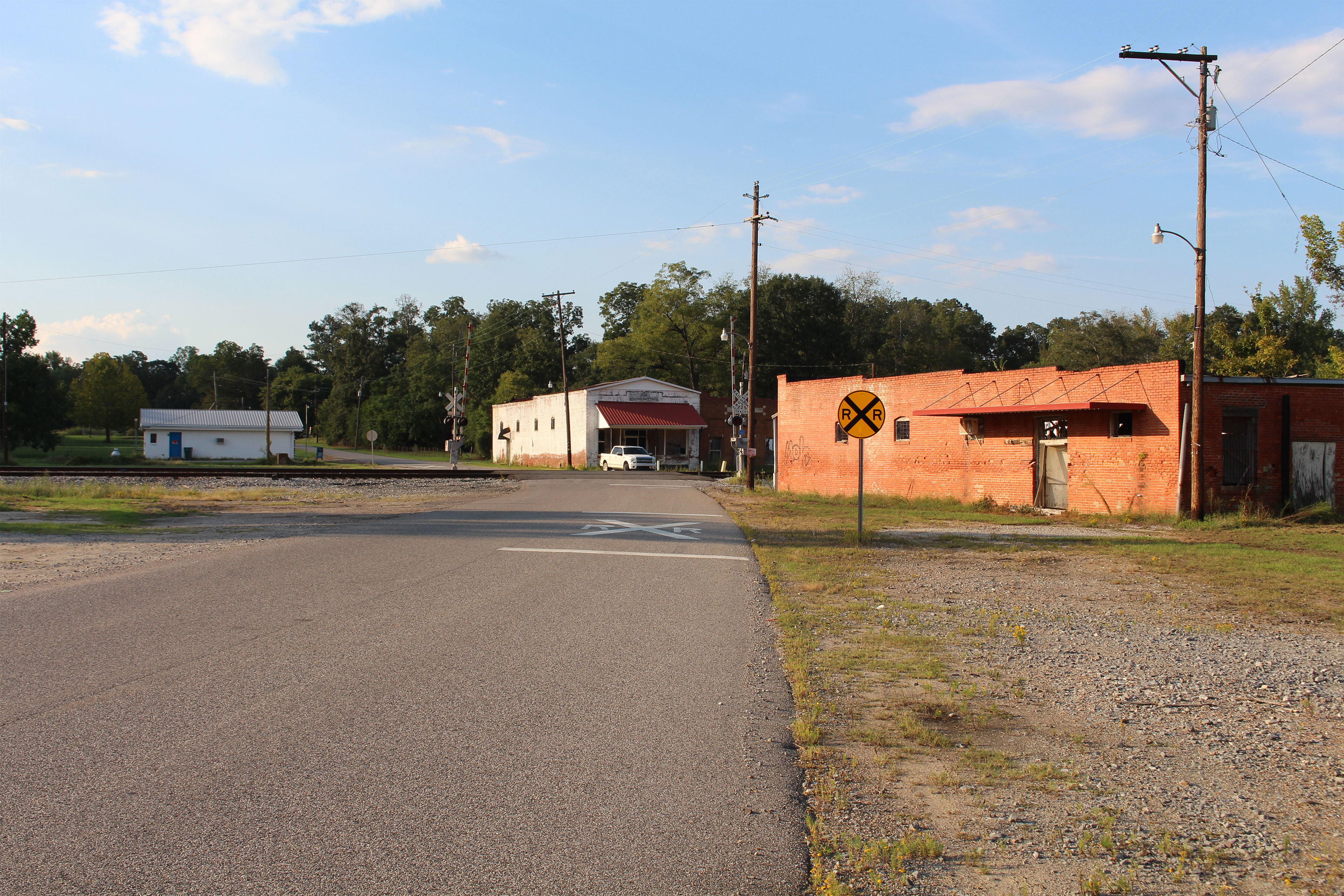 The train crossing of a rural road surrounded by three low buildings.