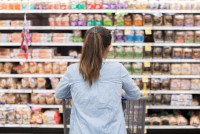 Rear view of woman shopping for bread in supermarket. She is standing in front of a large selection of bread.