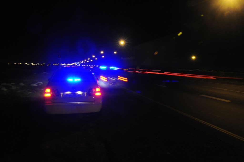 A photo taken at night of two police cars with blue flashing lights driving on a highway.