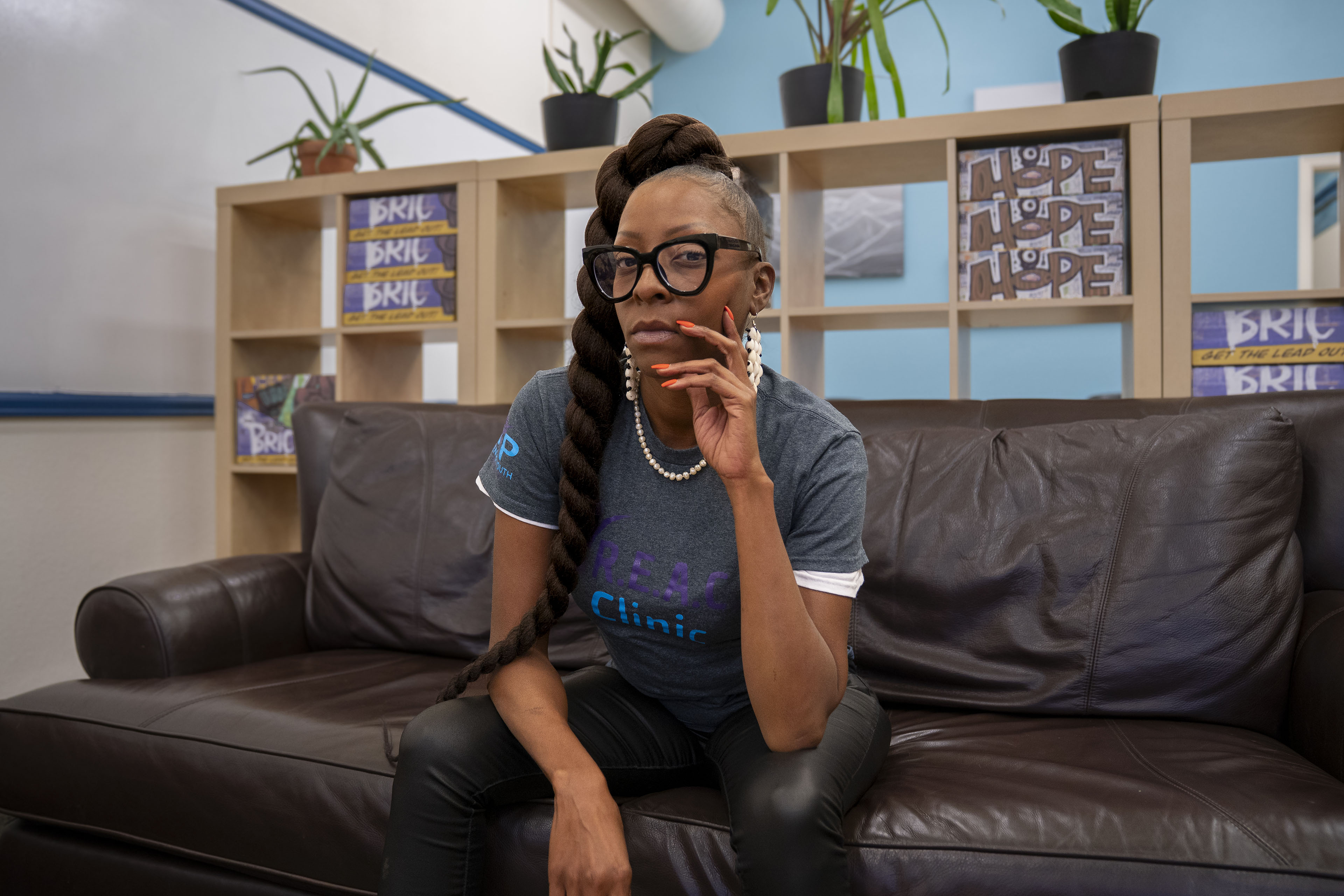 A woman sits on a leather couch and holds her chin in her hand thoughtfully while looking towards the camera.