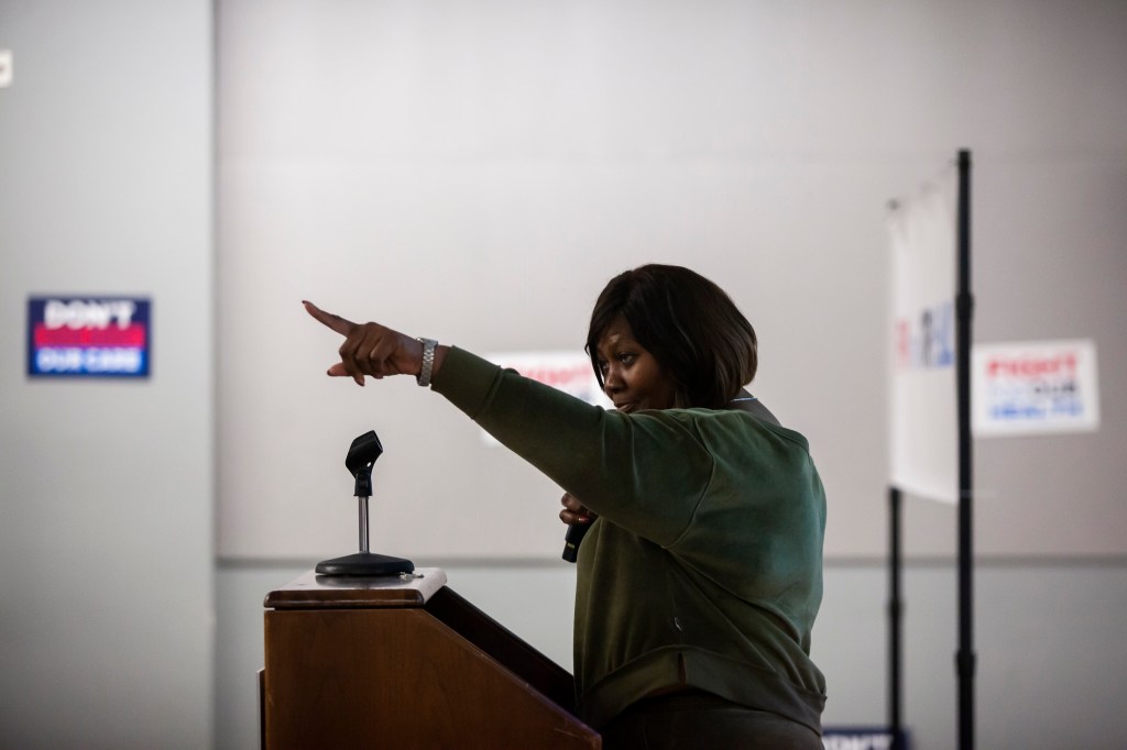 A woman wearing a green sweater stands at a podium and points into the audience.