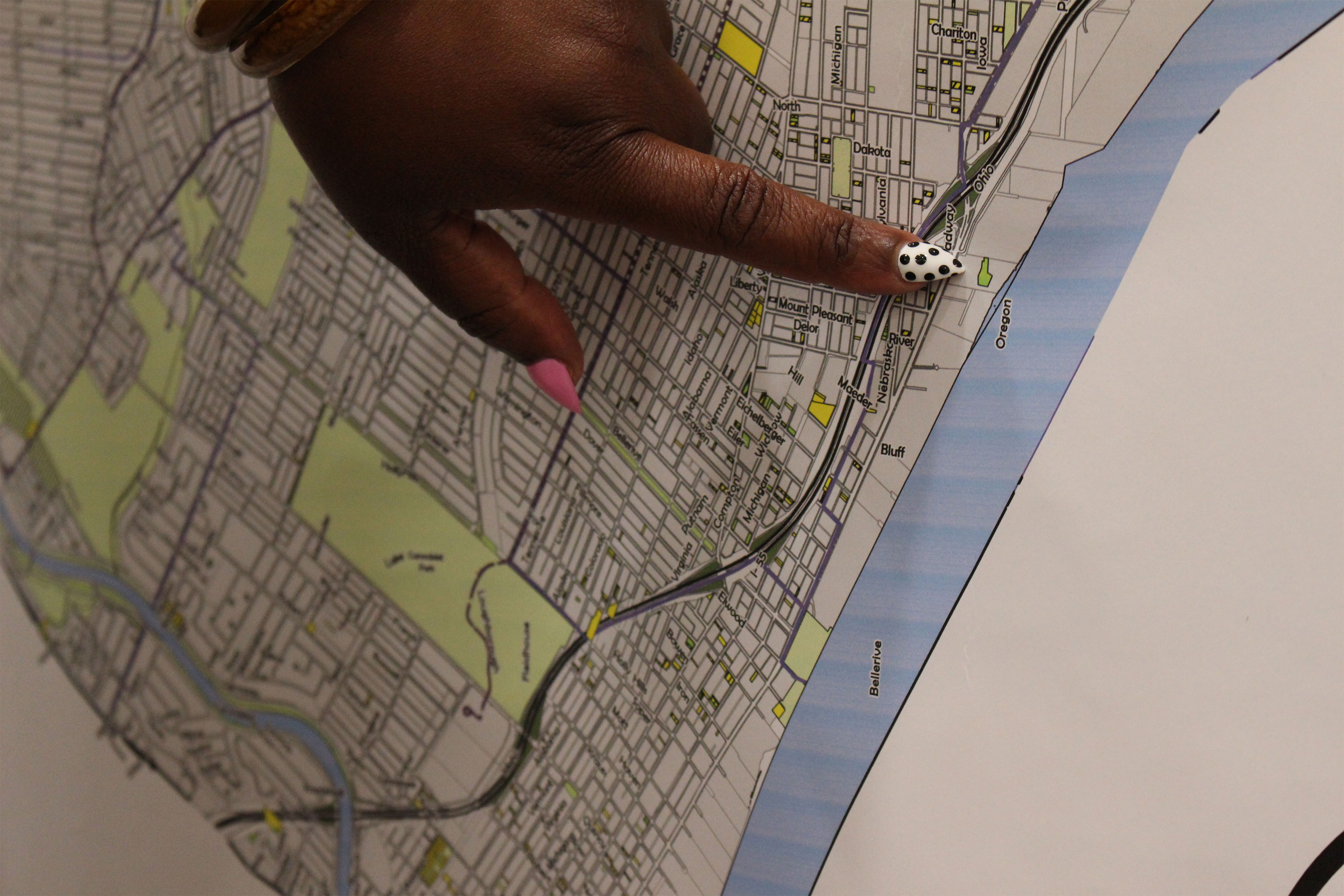 A close-up image of a hand point to a location on a map. The index finger nail is painted white with black dots and the thumb nail is painted pink.