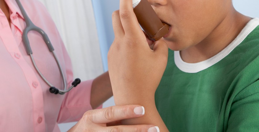 A photo of a nurse helping a young boy use an asthma inhaler.