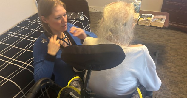 A photo of a nurse practitioner examining an older woman patient in her home.