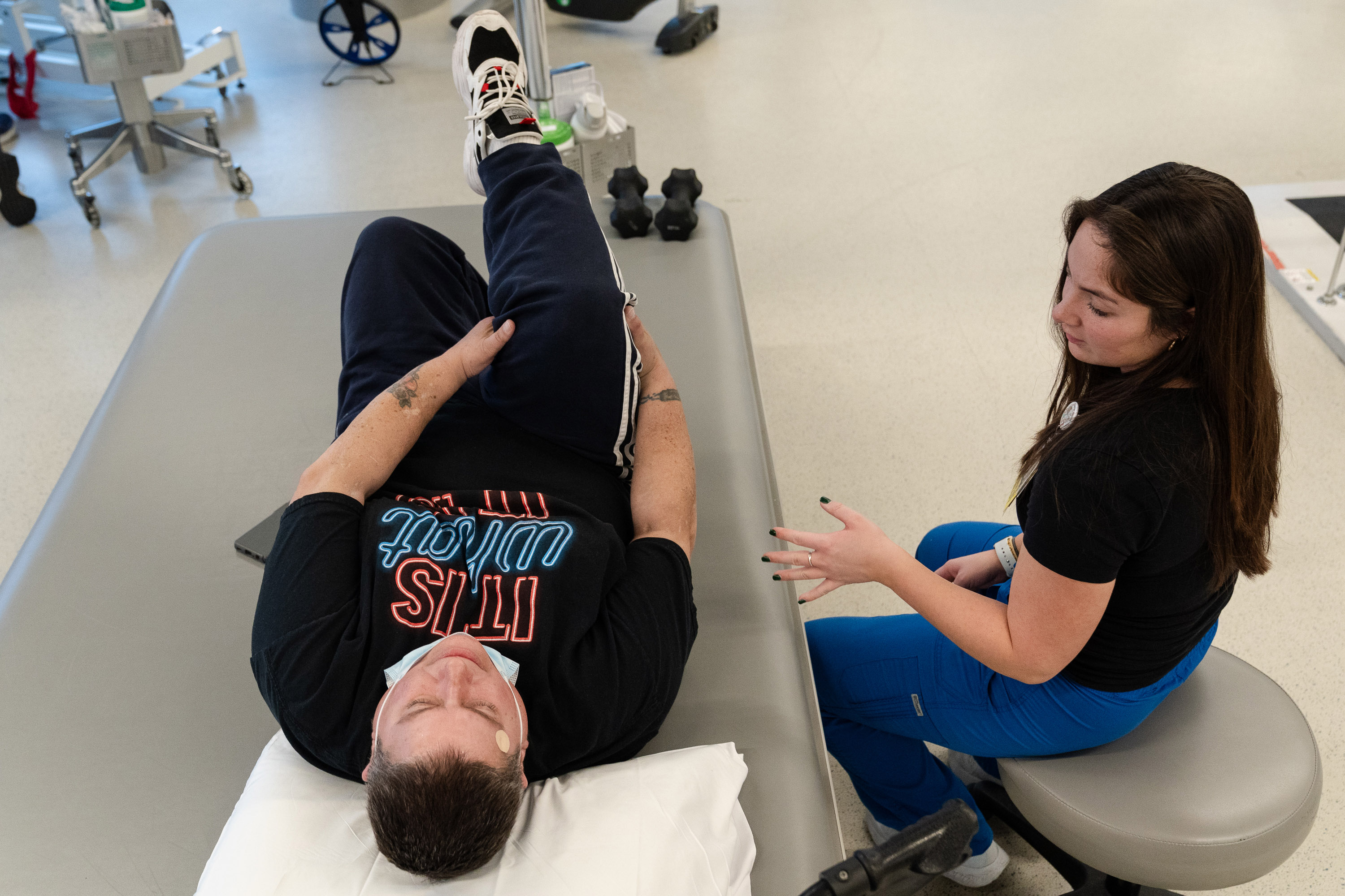 A woman sits next to a man who is stretching his leg