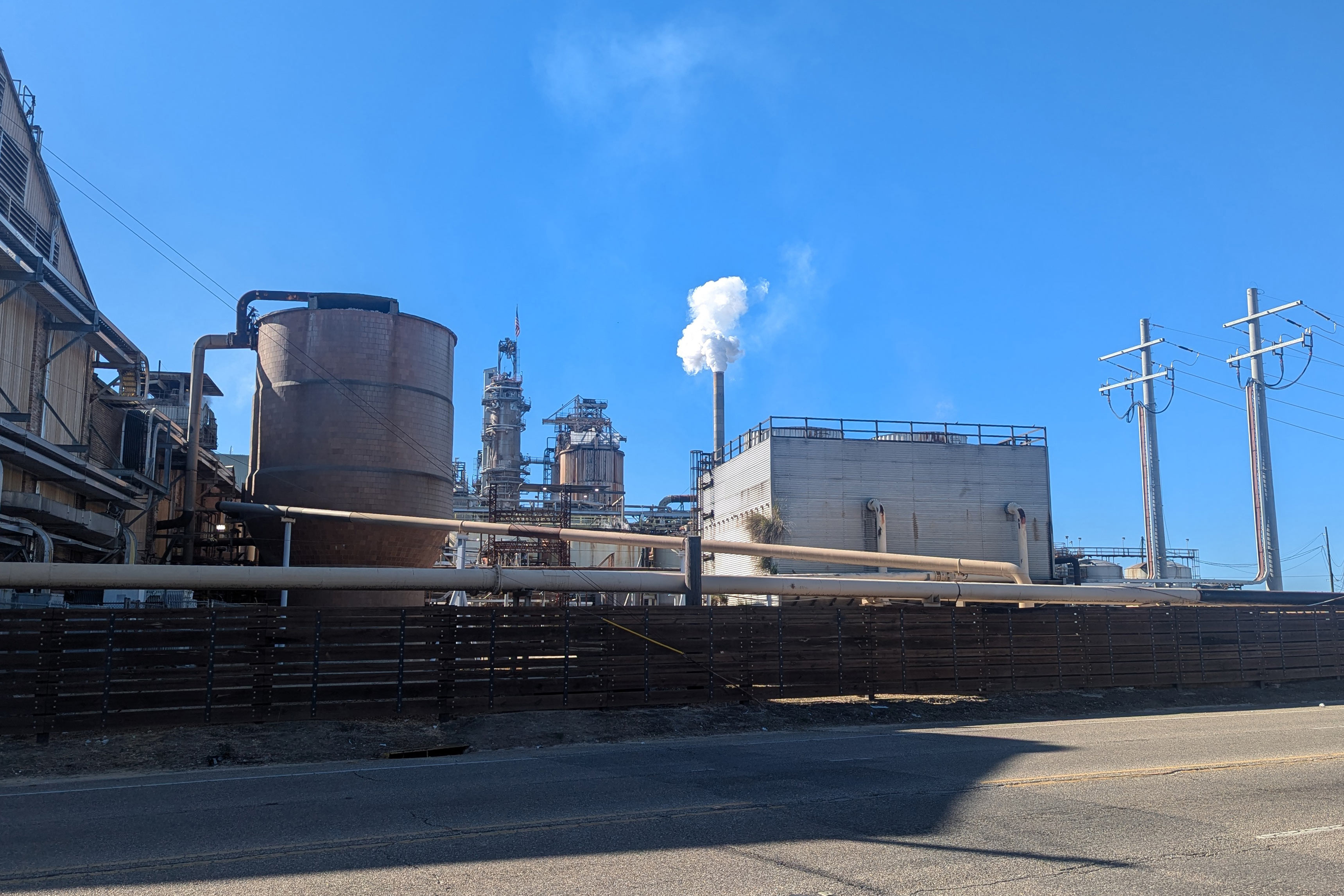 A photo of the exterior of a large mill. Smoke or steam billows out of one of a cooling tower.