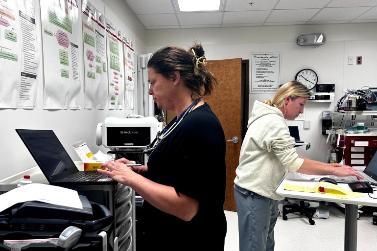 Two female medical professionals stand in an office typing on laptops