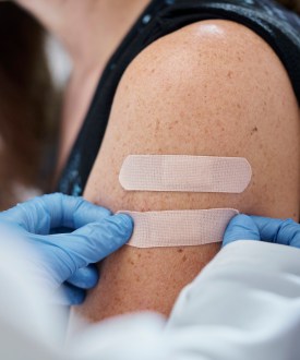 A close-cropped shot of a doctor wearing blue gloves giving second adhesive bandage to a young woman after administering vaccines.