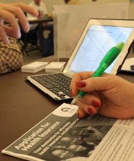 A photo of a laptop on a table. In the foreground is a woman holding a pen over a Covered California information packet.