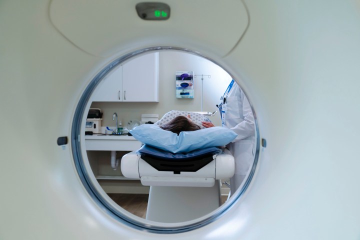 A doctor stands beside a patient about to go through a CT scanner, just out of view.