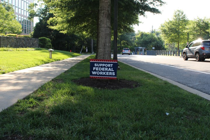 A lawn sign near a sidewalk reads, "support federal workers."