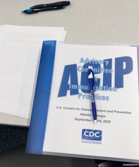 A binder rests on a table. The cover reads "Advisory Committee on Immunization Practices" and has the CDC logo on it.