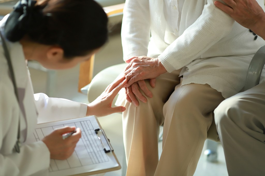 A young doctor checks her elderly patient's knee.