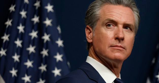 A photo of Gov. Gavin Newsom at a news conference with an American flag behind him.